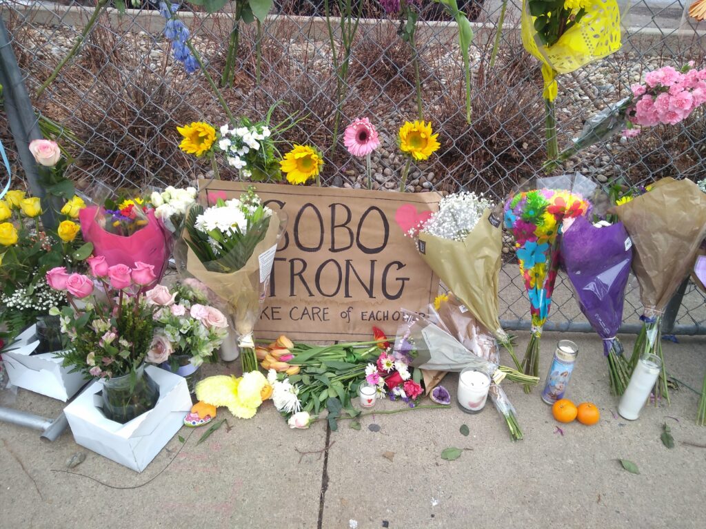 A photo of the memorial outside the Table Mesa King Soopers, with flowers and a sign saying SoBo Strong.
