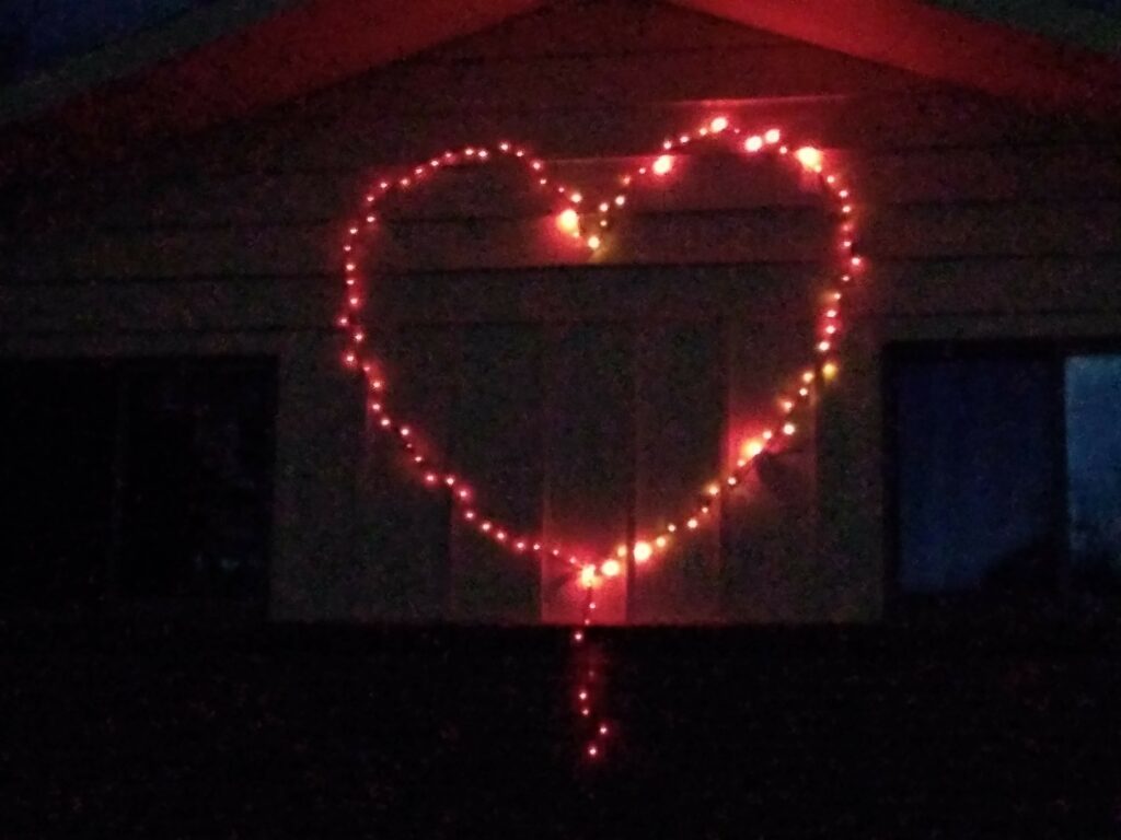 A string of red holiday lights in the shape of a heart on the front of a house